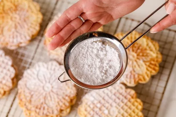 sprinkling domino powdered sugar on pizzelles cookies